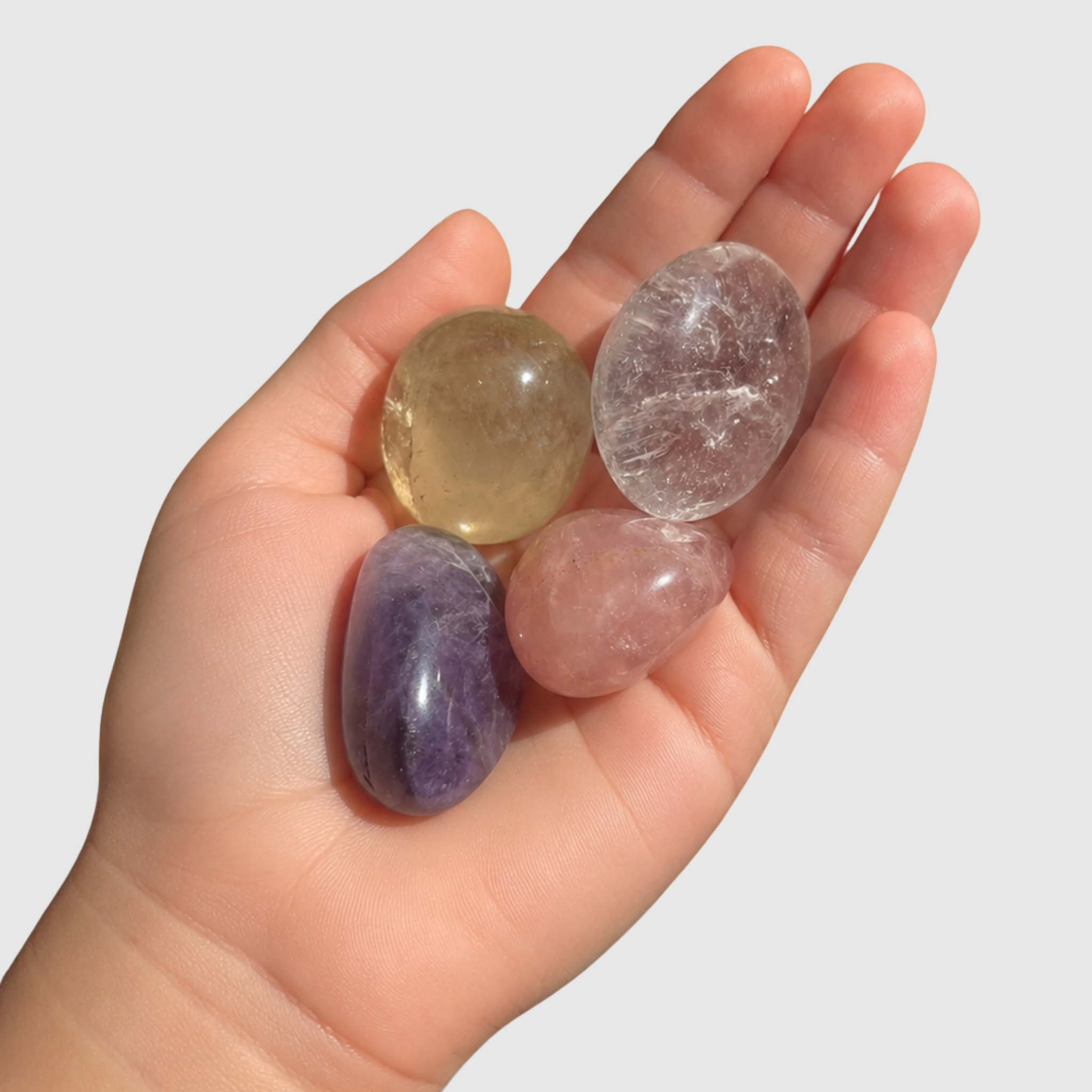 Kinderhand hält vier bunte Edelsteine – Rosenquarz, Citrin, Amethyst und Bergkristall